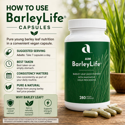 A bottle of AIM BarleyLife capsules with a green label, shown beside informational text and several capsules on a wooden surface. The scene includes a blurred green plant background and promotional copy about using BarleyLife capsules.