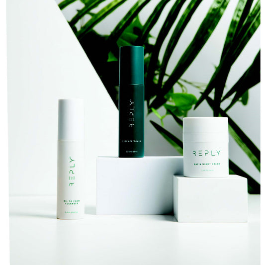 AIM Reply skincare trio featuring Oil to Foam Cleanser, Essence/Toner, and Day & Night Cream displayed against a green botanical background.